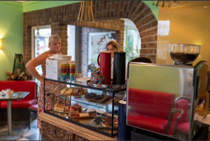 Kundin steht neben der Kuchentheke in einem liebevoll eingerichteten Blumen Kunst Café.