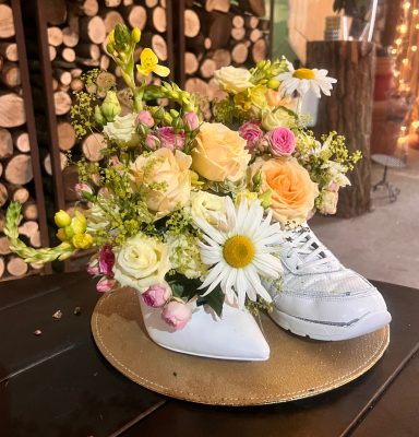 Blumengesteck zur Hochzeit in weißem Damenschuh und Herrensneaker auf einem goldenen Teller.