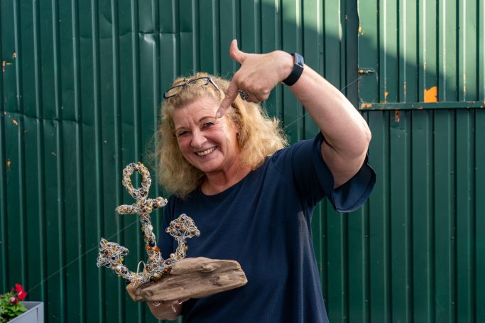 Die Künstlerin Geli Rybarczyk mit ihrem Kunstwerk aus Treibholz vom Rheinufer und einem aus Draht und Perlen geformten Anker.