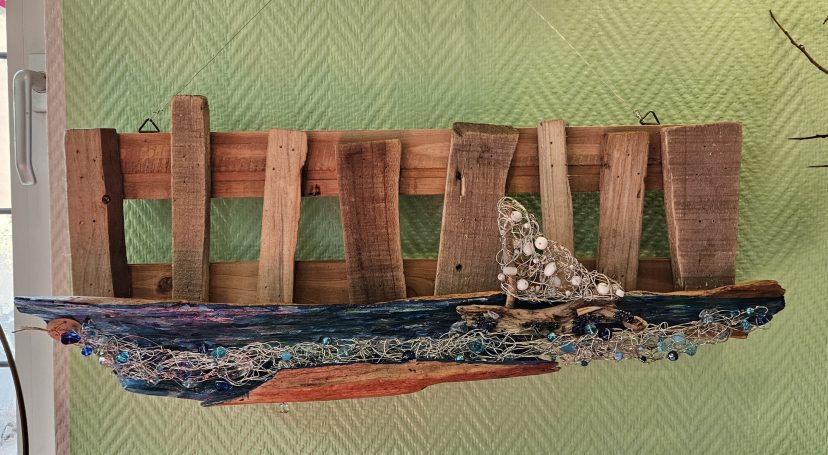 Ein Wandschmuck Kunstwerk aus Treibholz vom Rheinufer und einem aus Draht und Perlen geformten Schiff.