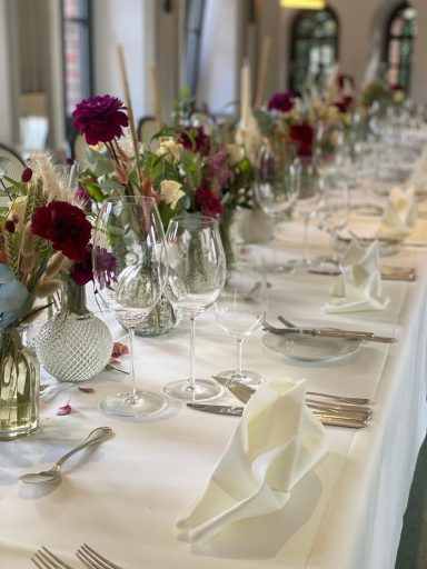 Tischdeko zur Hochzeit mit vielen verschiedenen Vasen und kleinen Rosensträußchen auf langer gedeckter Tafel.